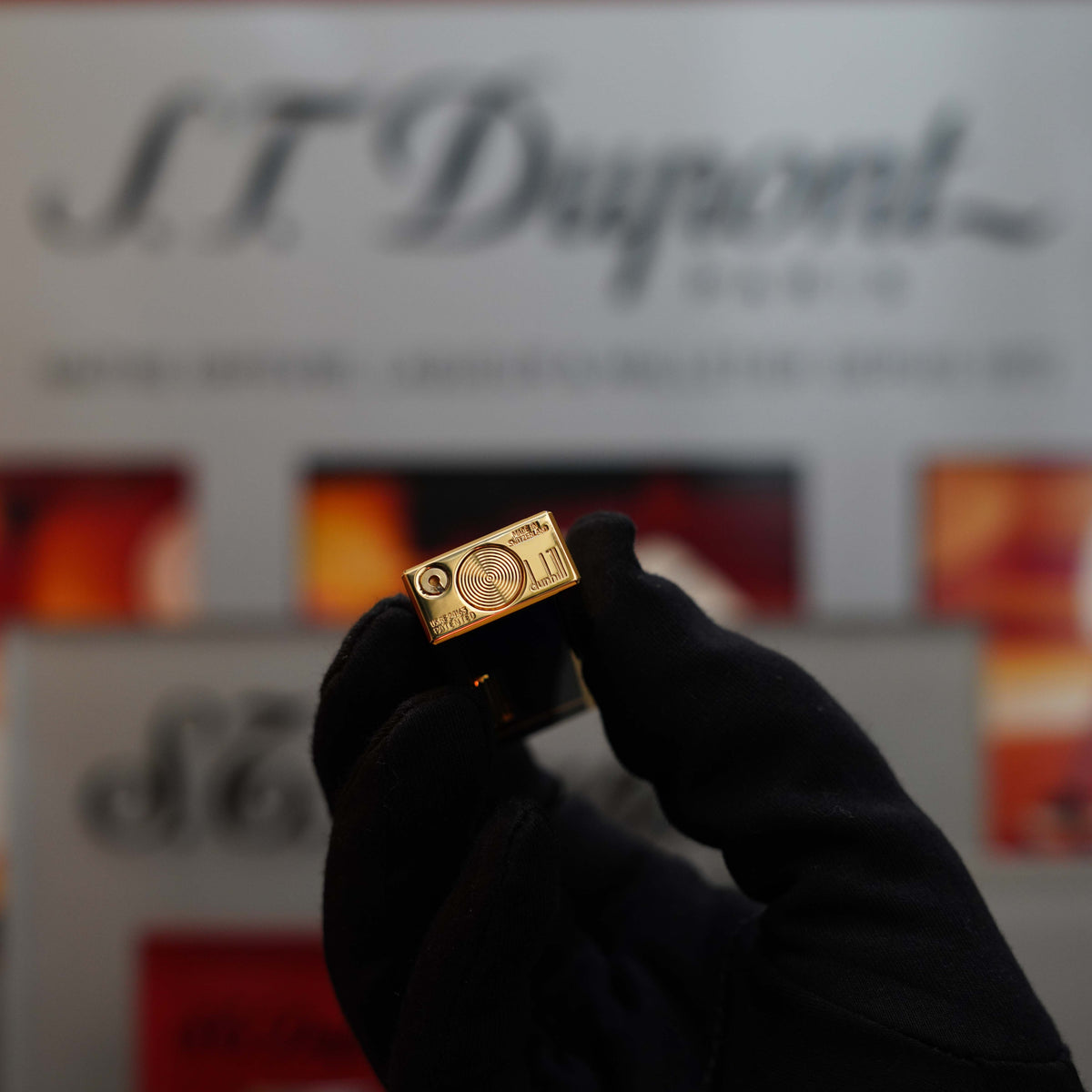 A gloved hand holds a gold-plated cufflink embossed with intricate designs, glowing with the same elegance as a Vintage 1980 Dunhill Rare Lapis Lazuli v2 24k Gold finish Rollagas Lighter. The background features blurred text and images on a display.