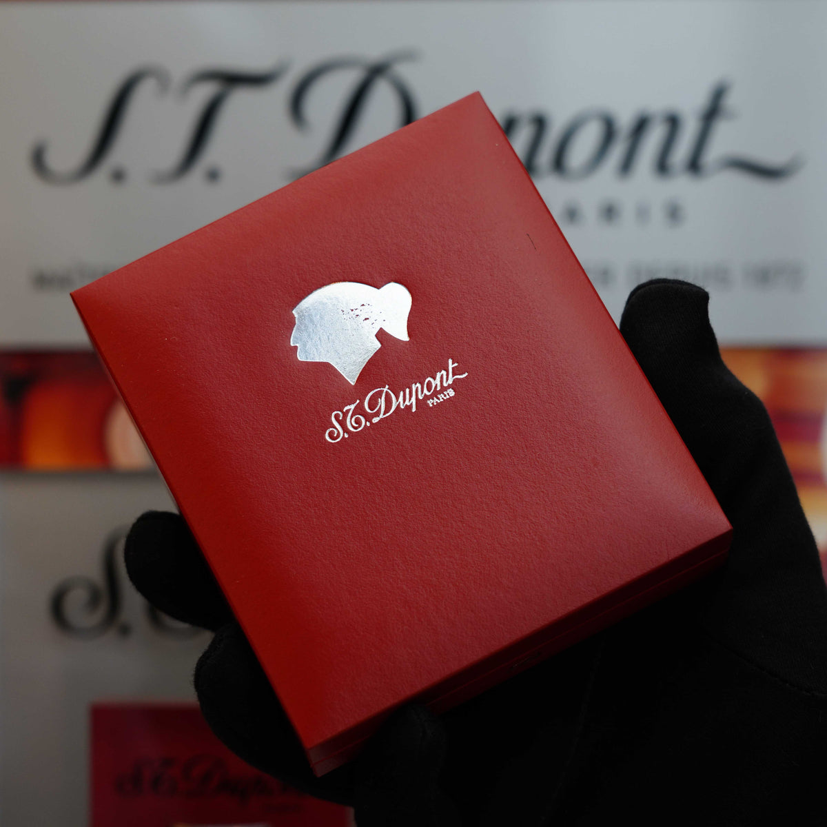 A gloved hand holds a red box featuring a silhouette and the logo "S.T. Dupont," revealing the timeless elegance of a Vintage 1992 rare St Dupont Cohiba First Edition Dual Flame Gatsby 24k Gold finish natural Lacquer lighter.