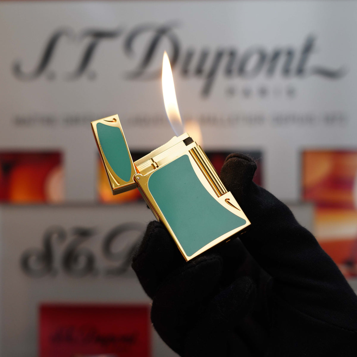 A gloved hand holding a lit, Vintage 1993 rare Art Nouveau early Limited Editions 24k Gold finish natural Green lacquer ligne 2 lighter in front of an S.T. Dupont branded background.