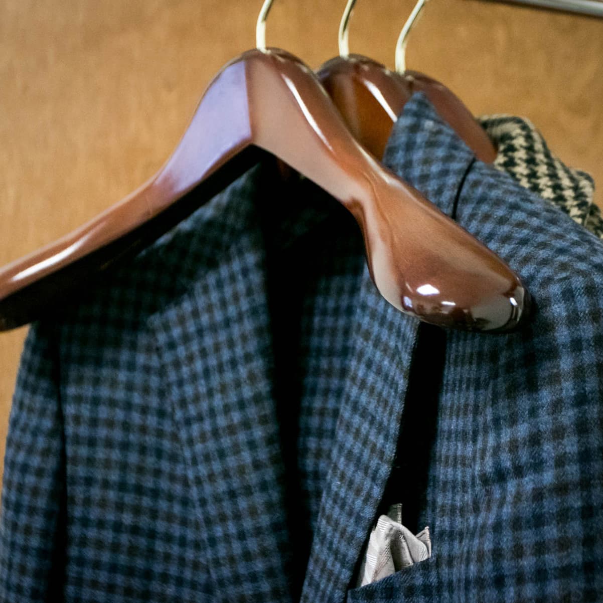 Image of a single brown wooden hanger, hanging in front of a navy and turquoise plaid suit jacket. 
