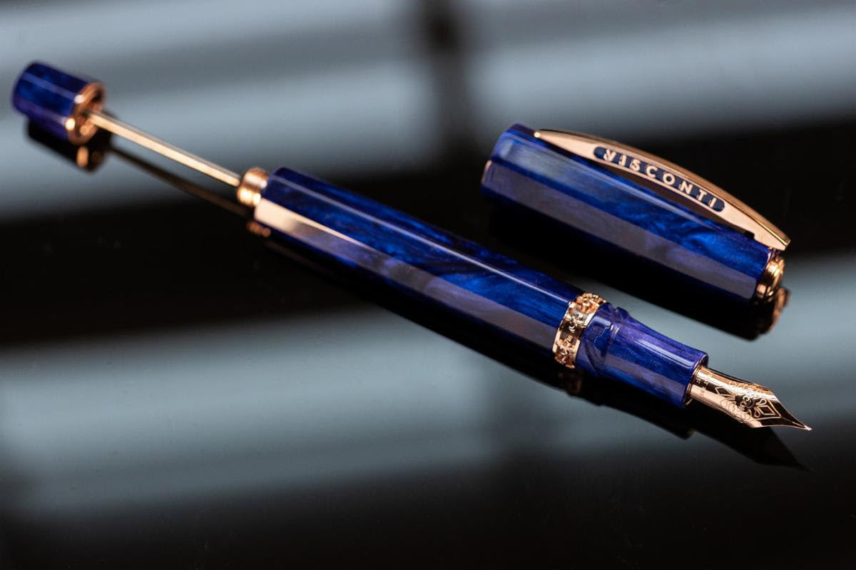 A blue Visconti Medici Viola Violet - Fountain Pen (18kt Gold Nib) with gold accents lies open on a black surface, showcasing its nib and cap. This limited edition luxury pen exemplifies elegance and craftsmanship.