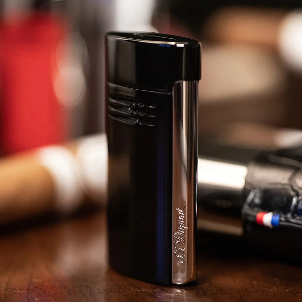 An S.T. Dupont Black Megajet Lighter sits on a table next to some cigars, showcasing its performance.
