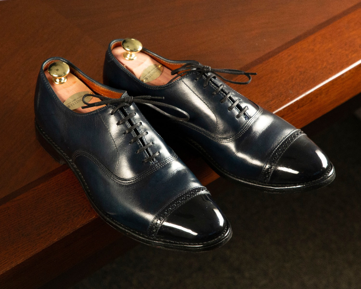 A pair of blue oxford shoes on a wooden table, showcasing the Presidential Shoe Shine Service by KirbyAllison.com.