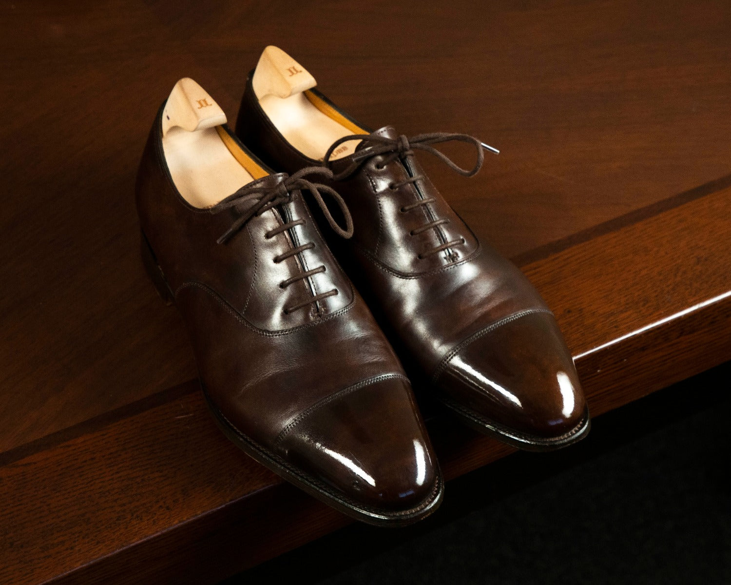 A pair of brown shoes on top of a wooden table with KirbyAllison.com's High Shine Service.