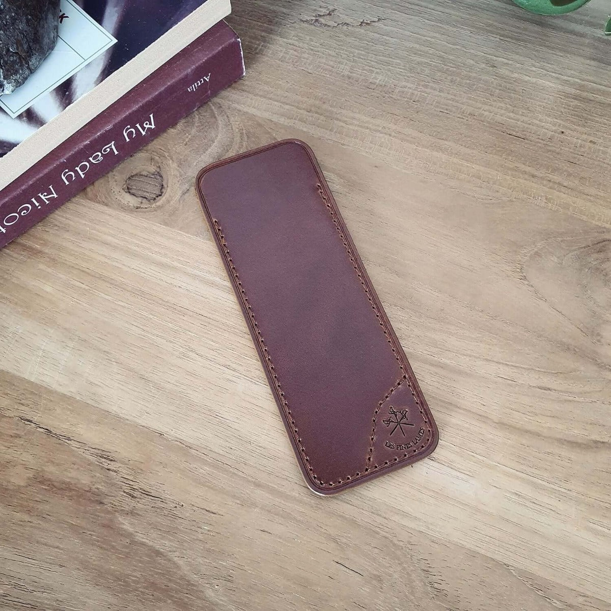 A Cigar Knife Tan Leather Case by KirbyAllison.com bookmark resting on a wooden table.