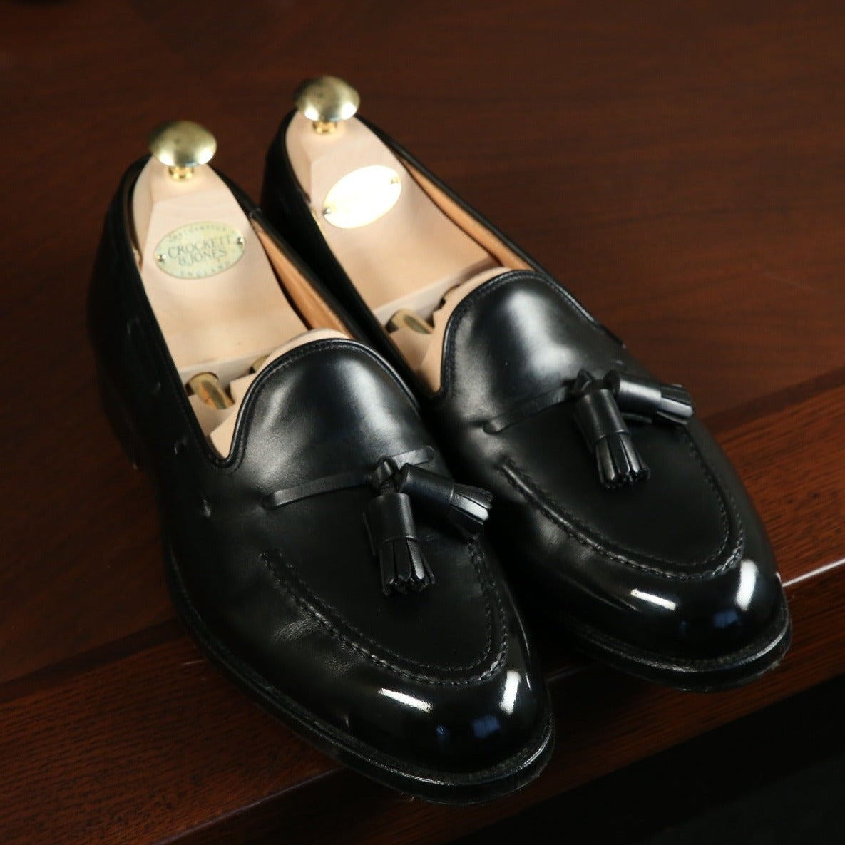 A pair of High Shine Service shoes from KirbyAllison.com with tassels sitting on a desk, highlighting shoe care.