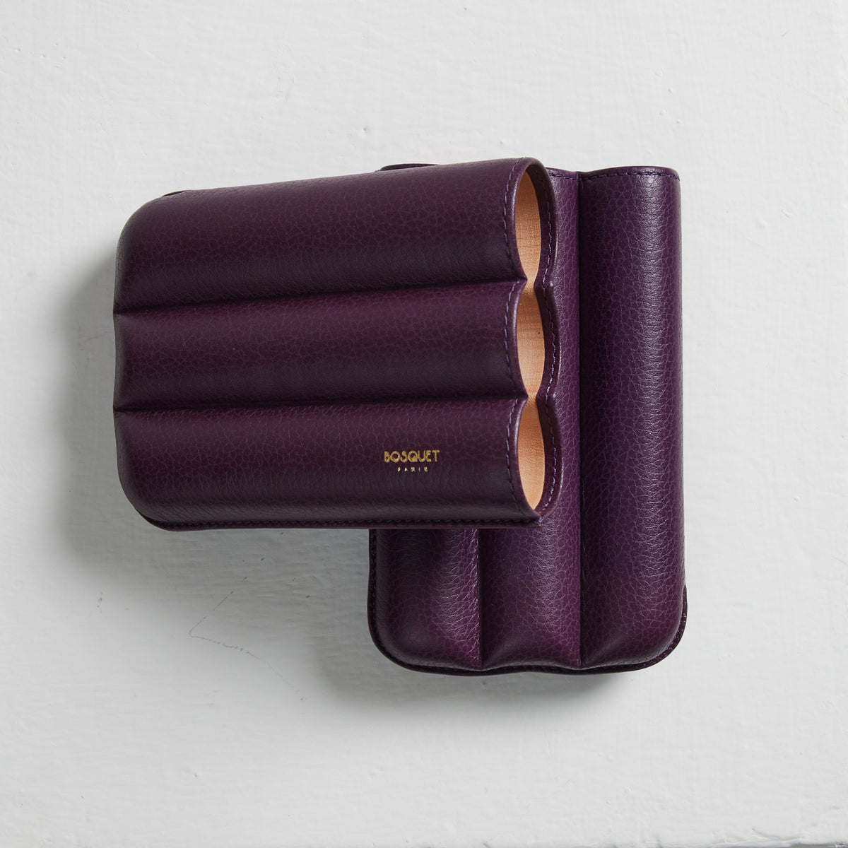 A Bosque Bosquet Smooth Purple Cylindrical Leather Cigar Case displayed on a white wall.