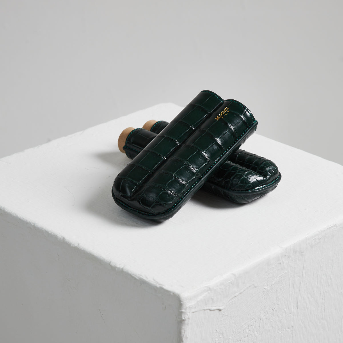 Two Bosque Bosquet Crocodile Cigar Case, Forest Green cases made of green crocodile leather are displayed on top of a white cube.