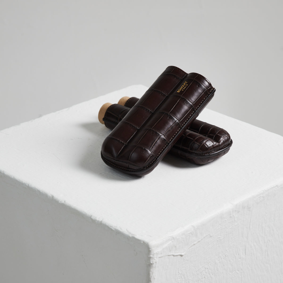 A pair of brown leather Bosque Crocodile cigar cases on a white cube.