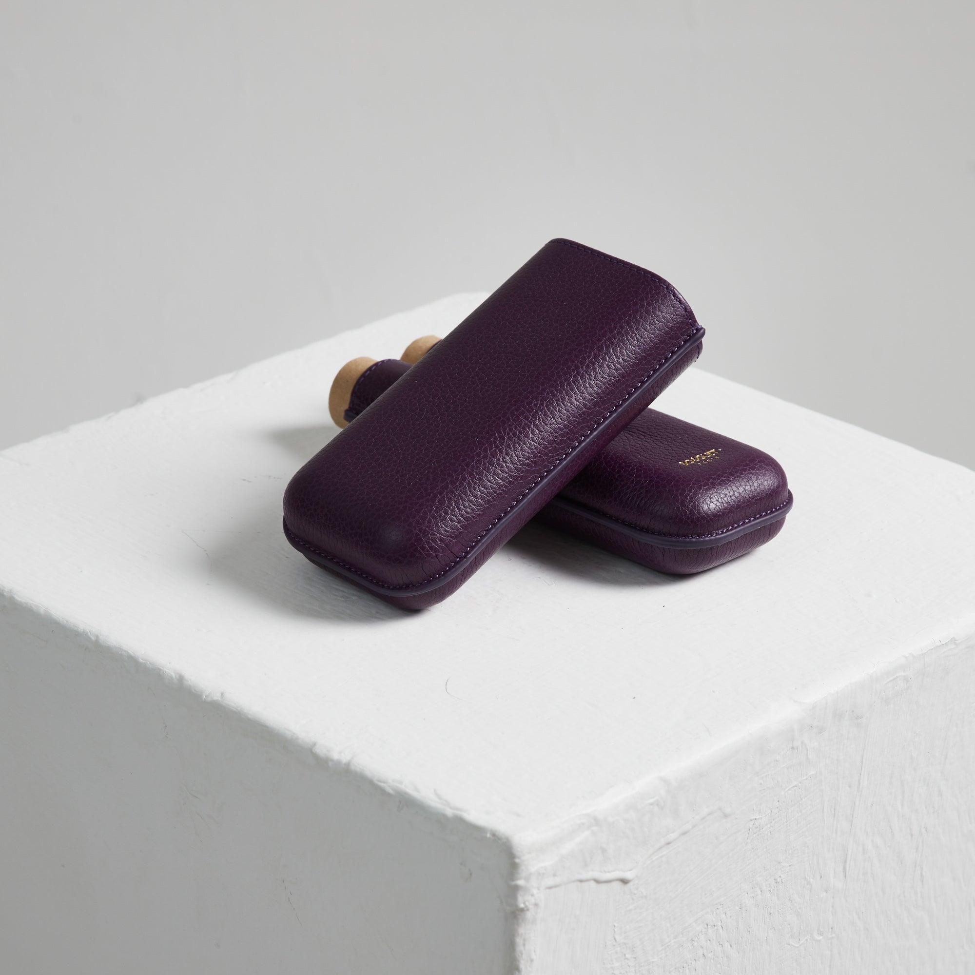 Two Bosquet Smooth Purple Leather Cigar Cases on top of a white cube.