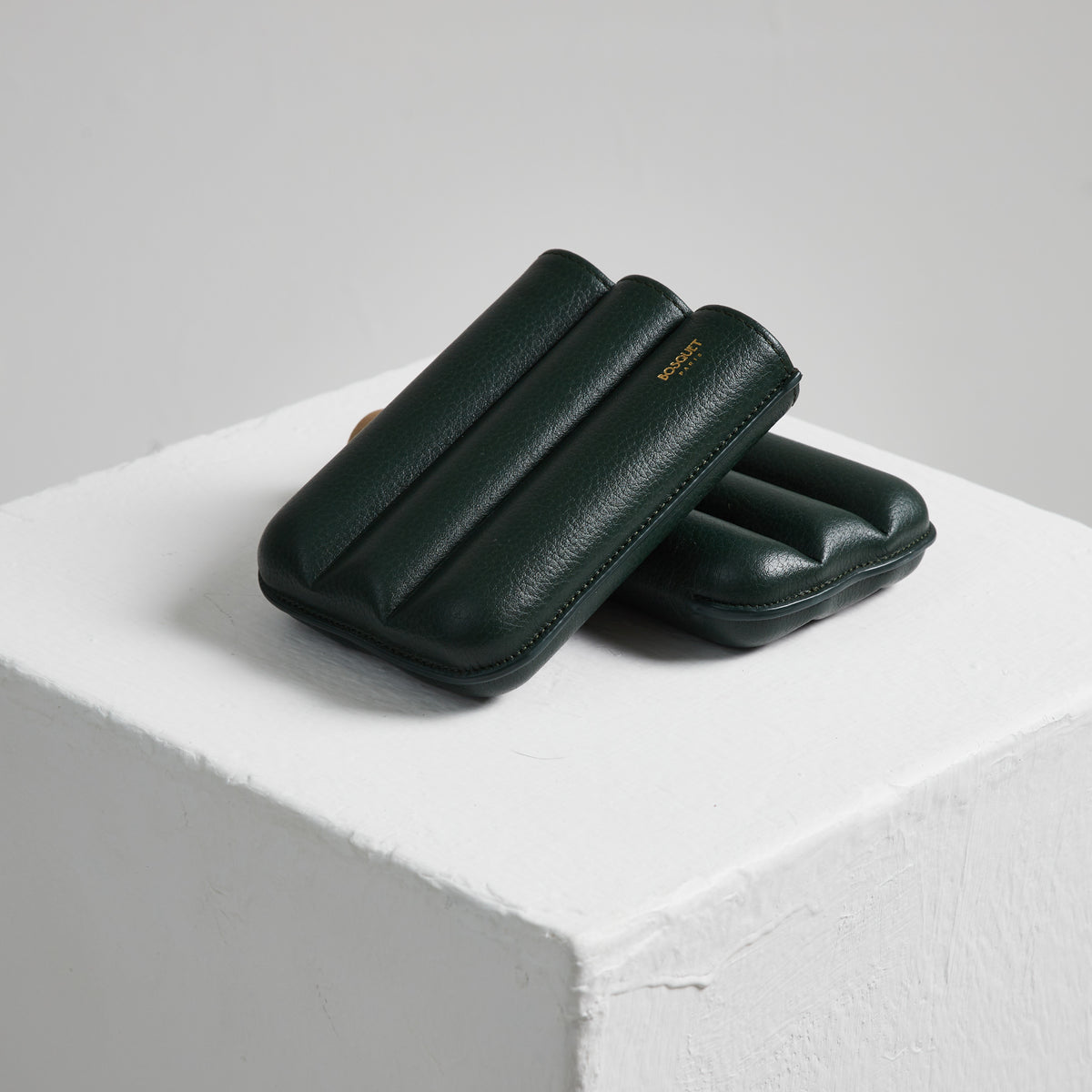 Two green Bosque cigar cases made with French leathers sitting on top of a white cube.