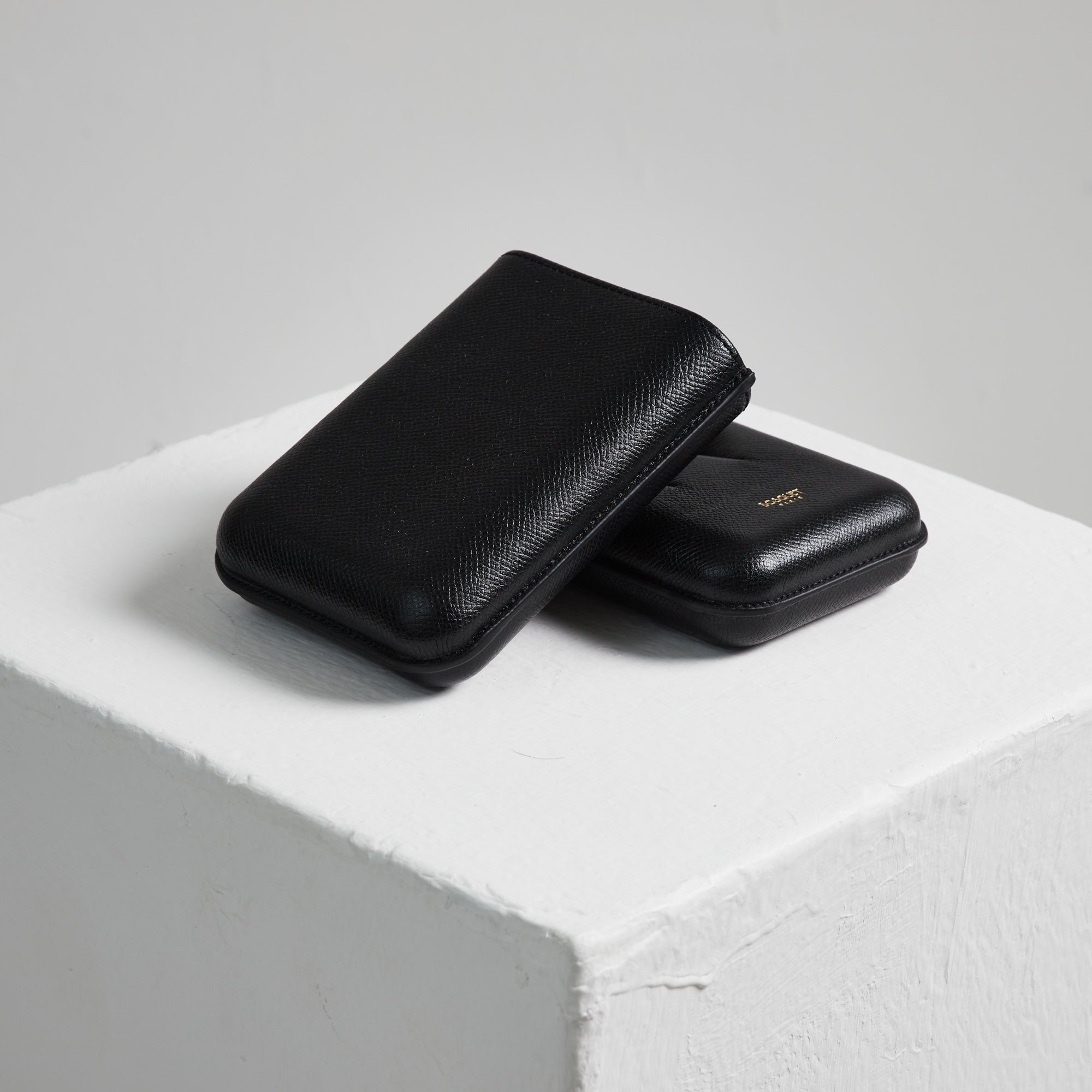 A black leather Bosquet Smooth Black Cylindrical Leather Cigar Case sitting on top of a white cube.