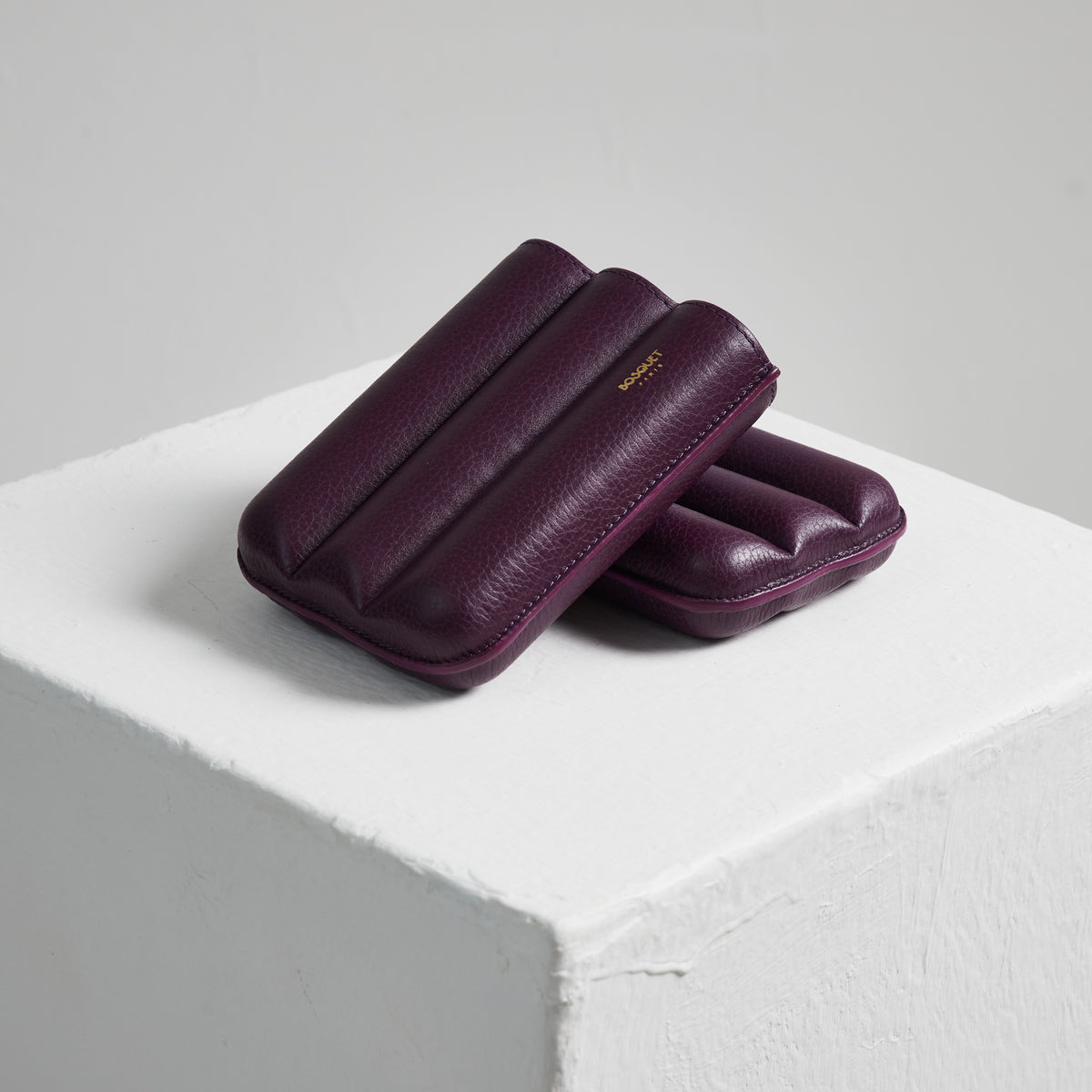 Two Bosque Smooth Purple Cylindrical Leather Cigar Cases sitting on top of a white cube.