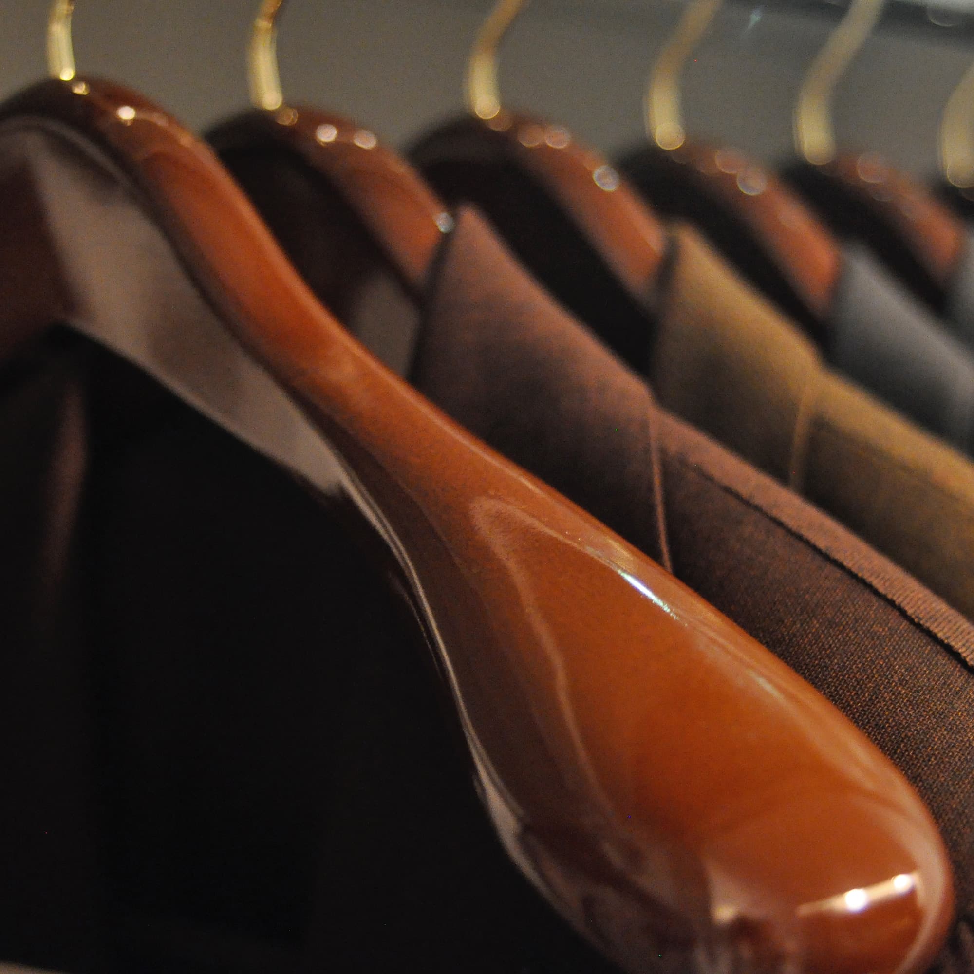Close up photo of glossy, brown wooden hangers with curved edges, arranged with dark jackets hanging along a bar, facing the viewer.