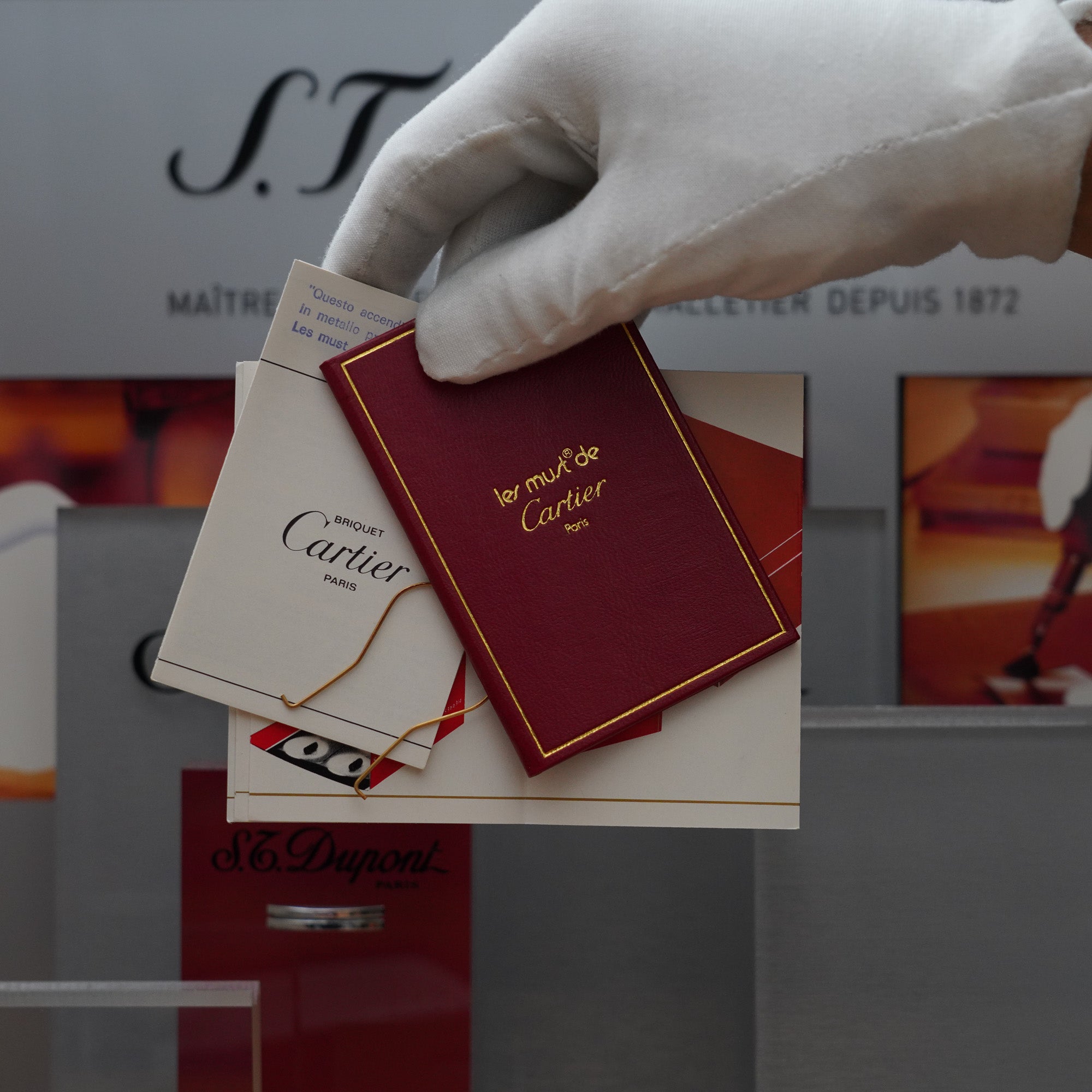 A hand is holding a Vintage 1980 Cartier Solid Silver 925 & Gold Factory iconic 18k Double C de Cartier logo lighter in front of a display case.