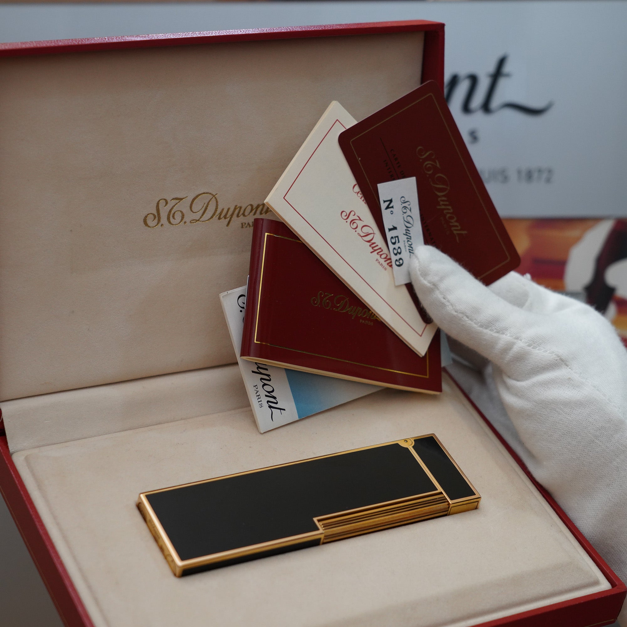A person is holding a Vintage 1980 S.T. Dupont 18k Gold Plated Ligne 2 Black Lacquer Table Lighter in a box.