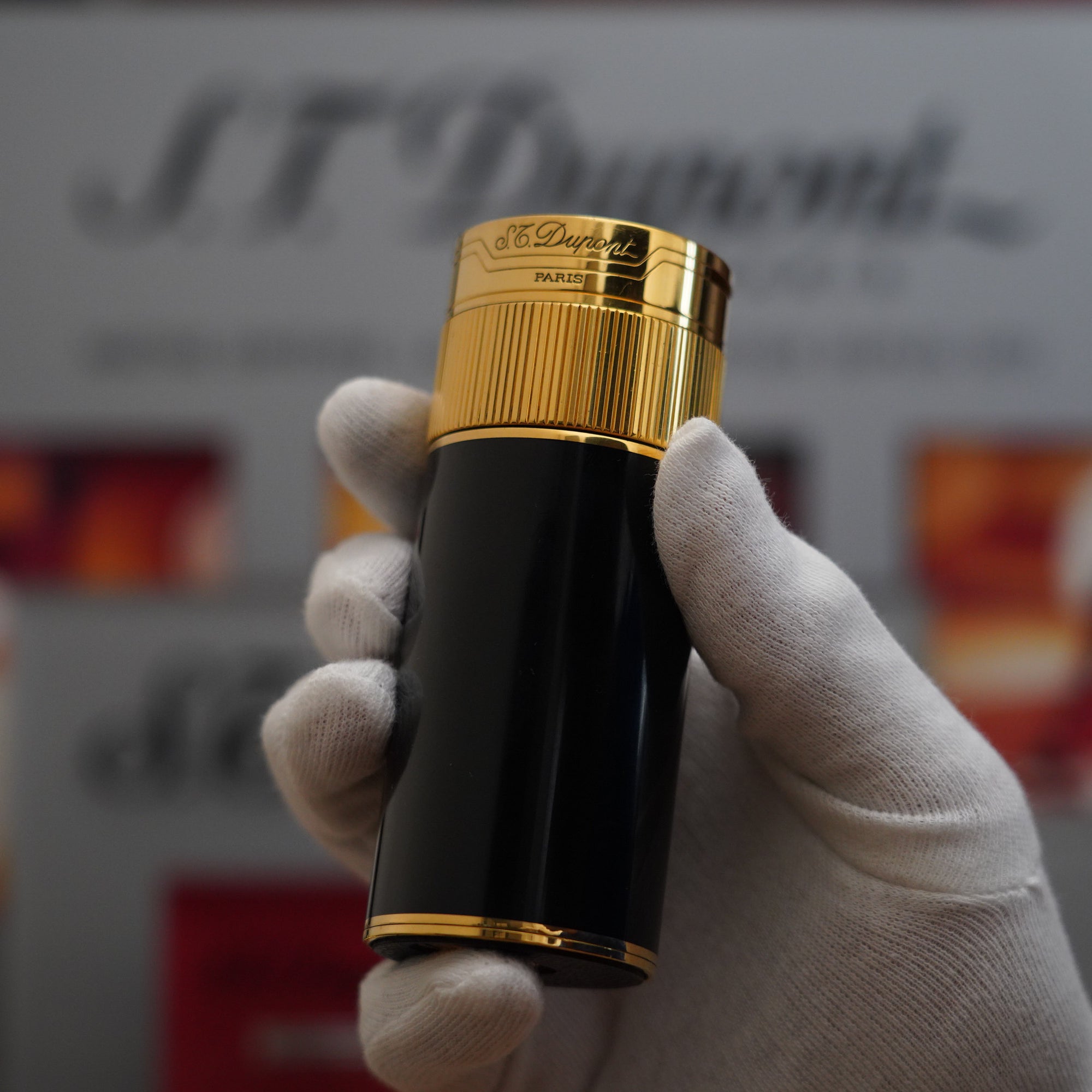 A person holding a Vintage 1980 S.T. Dupont 18k Unique Cylinder Gold Plated Black Lacquer Dual Flame Table Lighter.