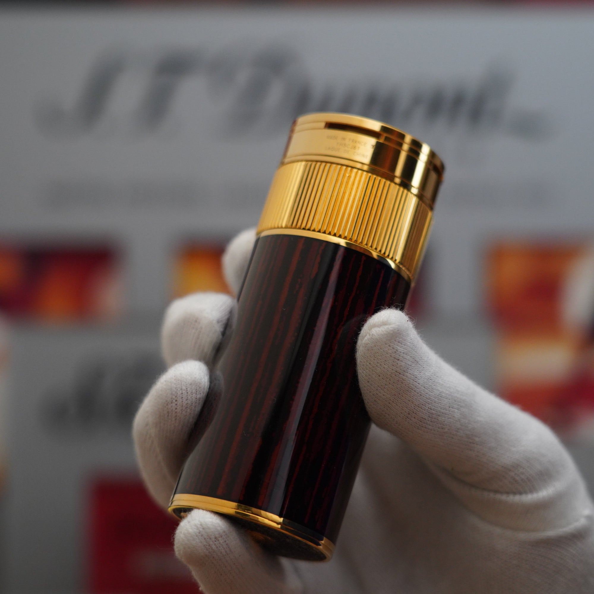A person holding a Vintage 1980 S.T. Dupont 18k Masterpiece Unique Cylinder Gold Plated Macassar Lacquer Dual Flame Table Lighter.