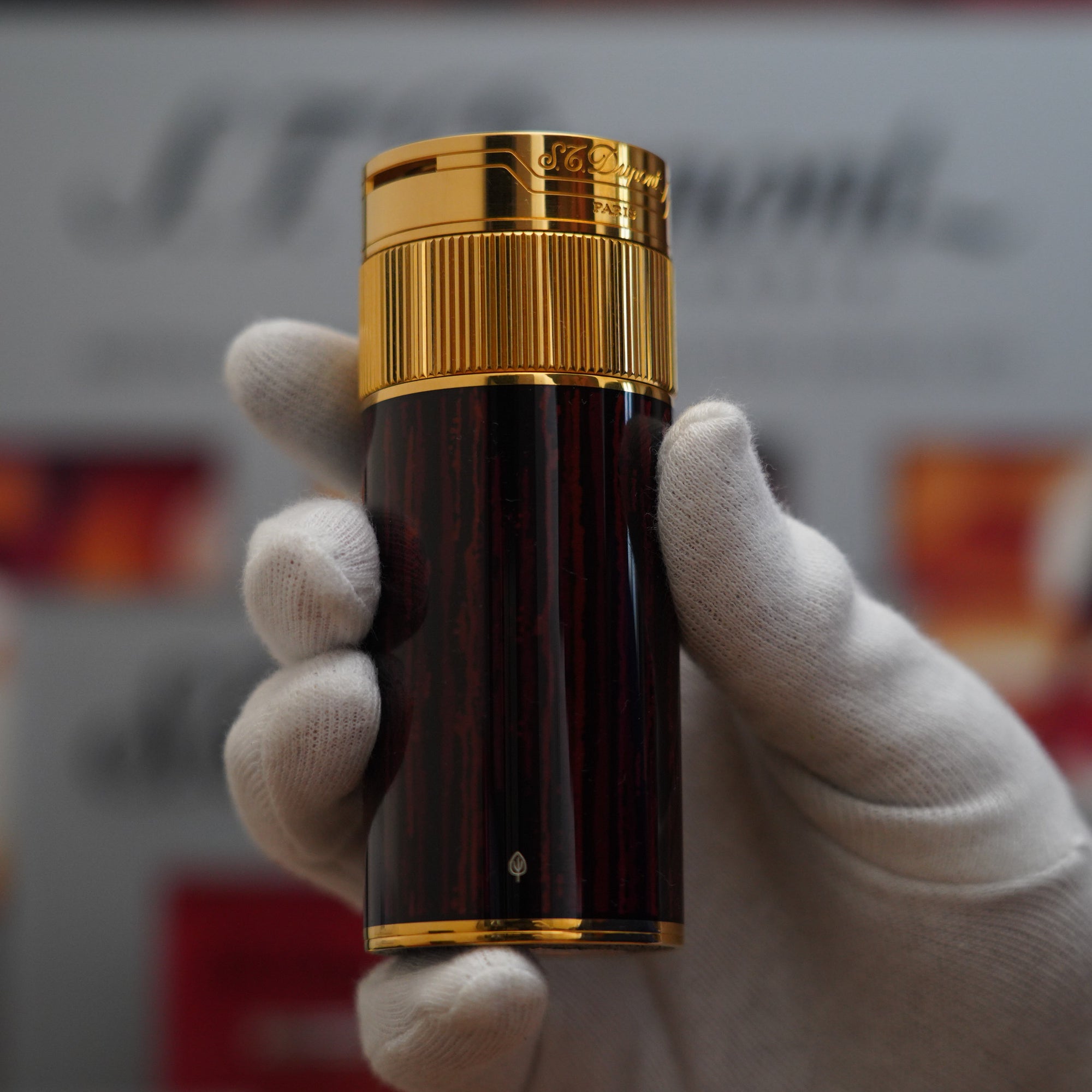 A person is holding up a vintage 1980 S.T. Dupont 18k Masterpiece Unique Cylinder Gold Plated Macassar Lacquer Dual Flame Table Lighter.