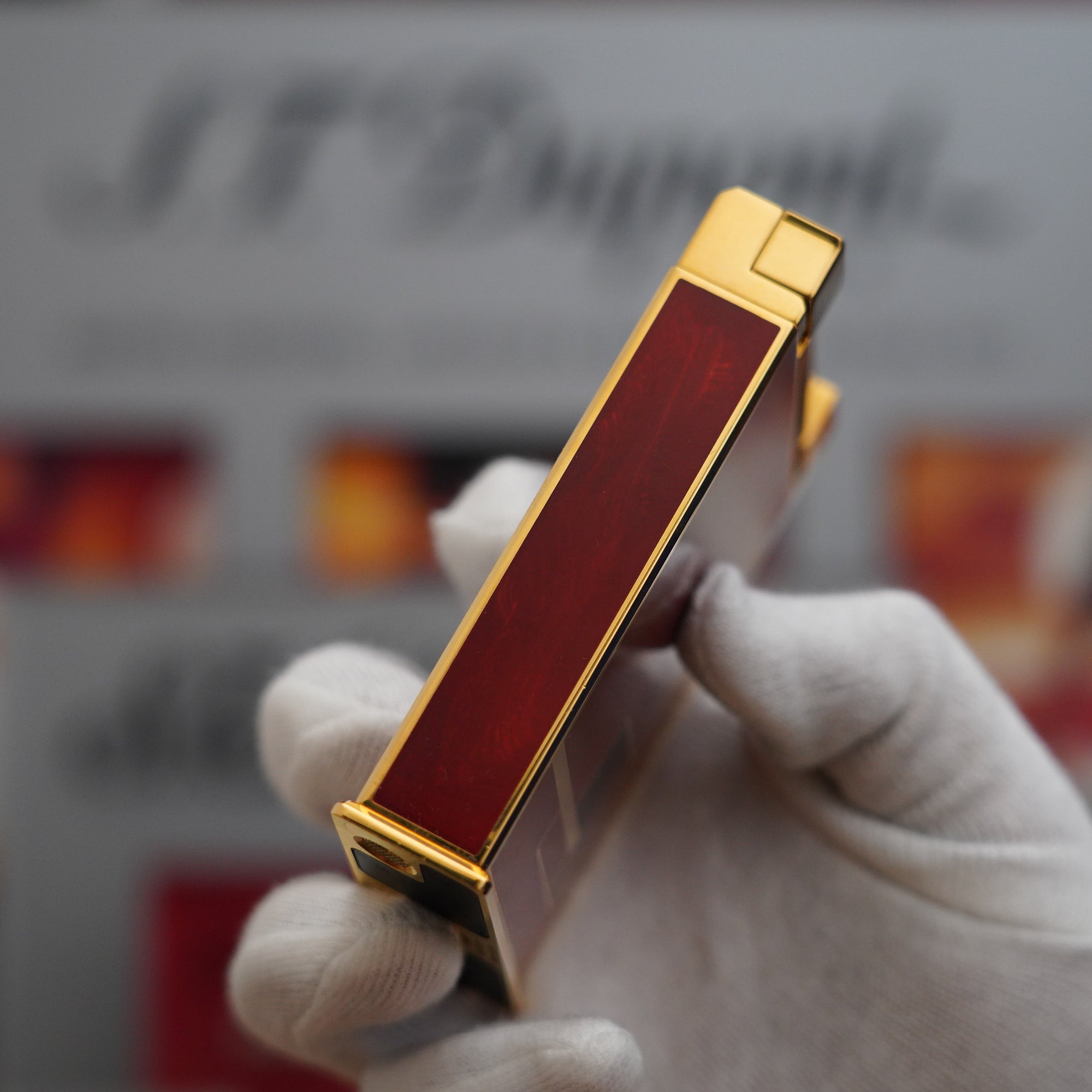 A person holding a Vintage 1990 S.T. Dupont 18k Jeroboam Gold Dust Red Chinese Lacquer Gold Plated Table Lighter box.