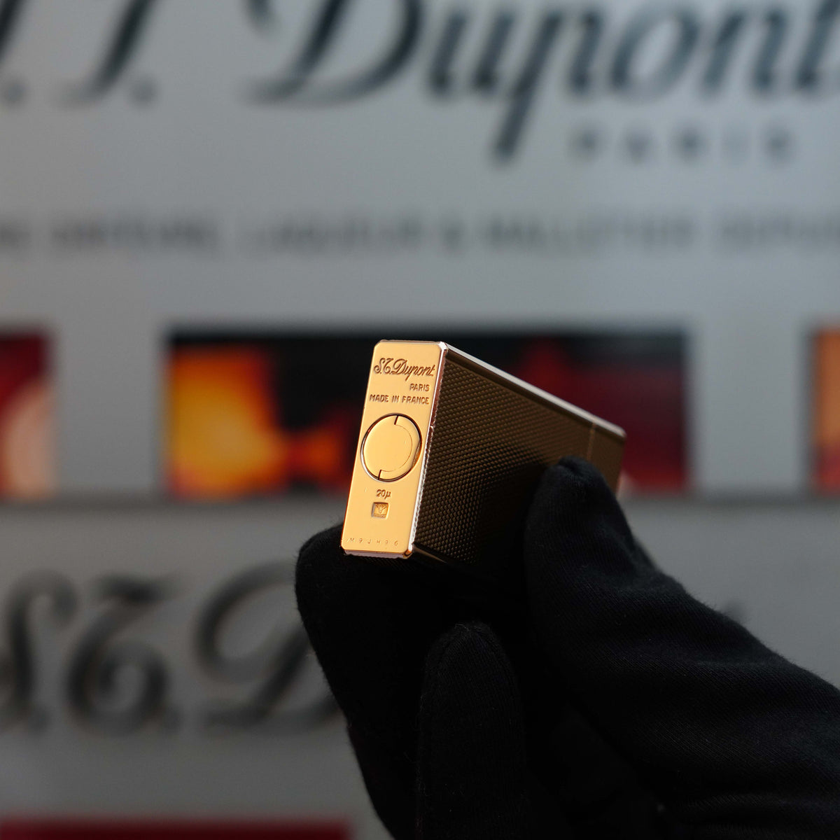 A gloved hand holds a silver and gold S.T. Dupont lighter against a blurred background, showcasing the distinguished Vintage 1970 St Dupont Micro Diamond rare Rose Gold Large Ligne 1 lighter. The S.T. Dupont brand name is visible, highlighting this vintage collector's item.