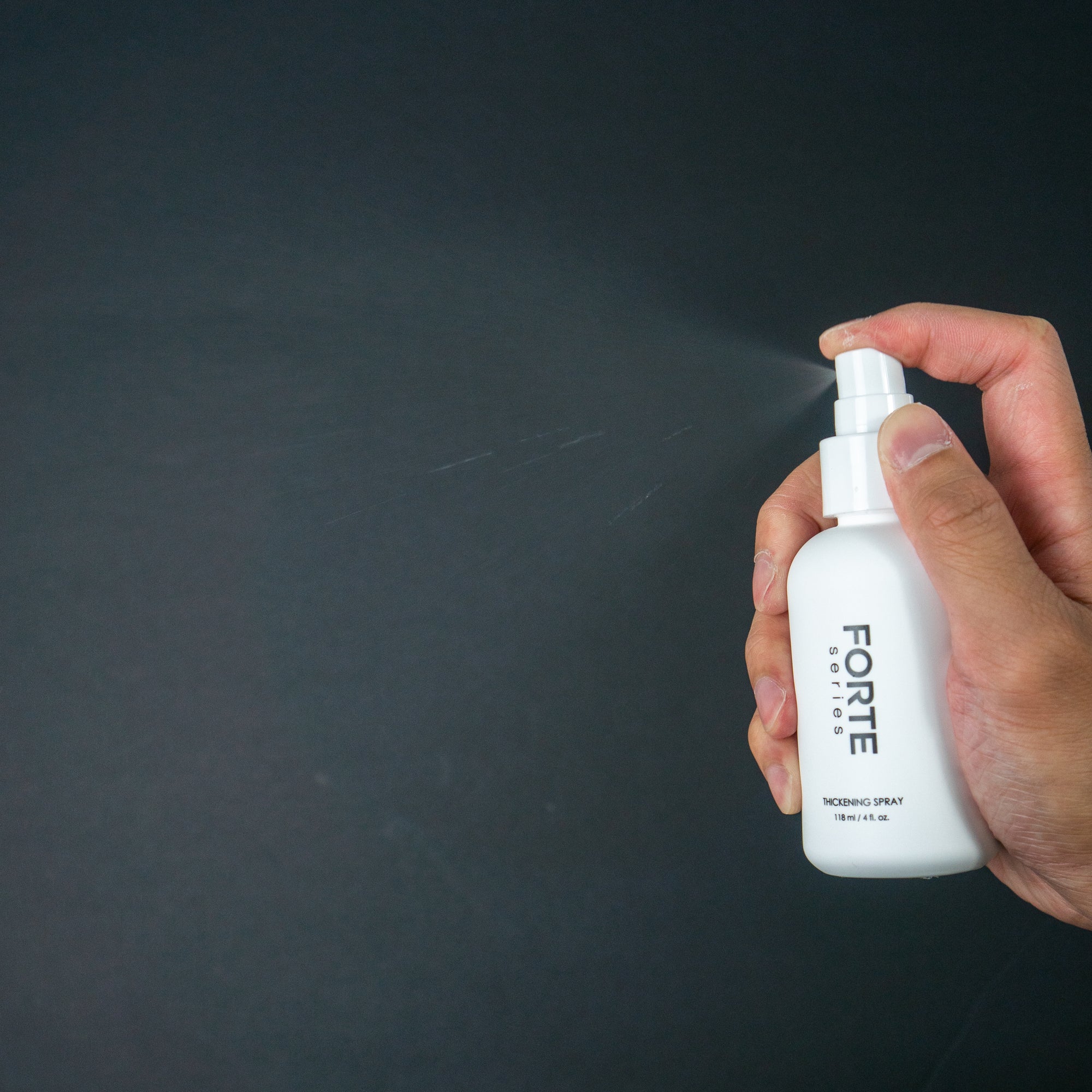 A hand holding a Forte Series Hair Thickening Spray, providing oil absorbing benefits for denser-looking head of hair with added body and volume, against a black background, by KirbyAllison.com.
