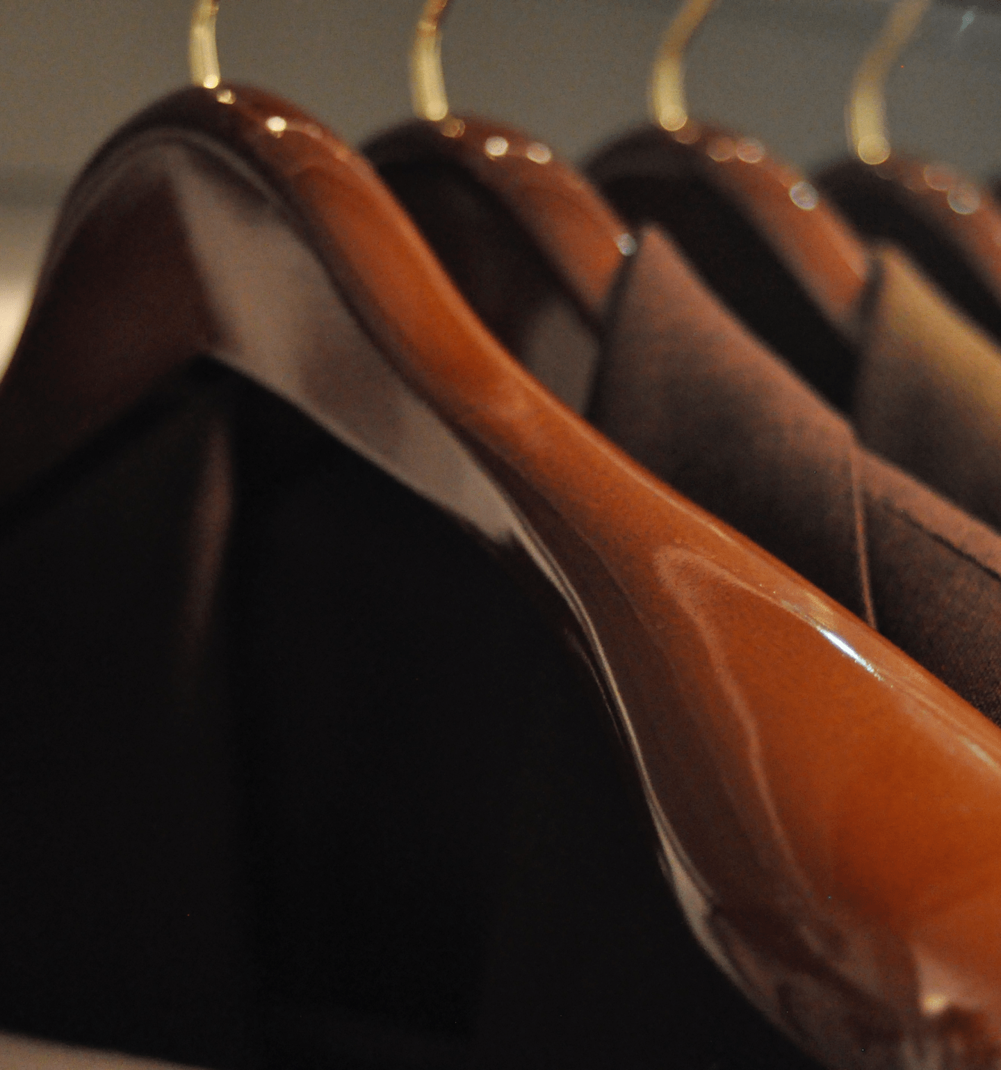 Close up photo of glossy, brown wooden hangers with curved edges, arranged with dark jackets hanging along a bar, facing the viewer.