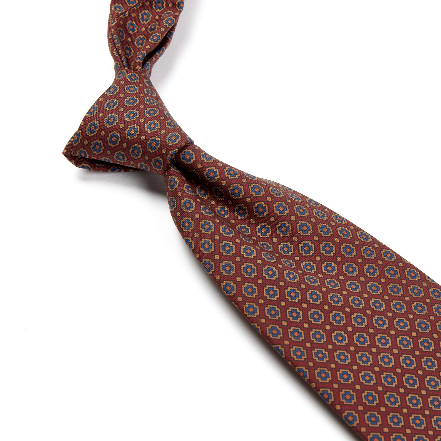 A handmade Kirby Allison Sovereign Grade Rust Small Floral Ancient Madder Tie with a circular pattern on a white background, showcasing the highest quality craftsmanship from the United Kingdom, available at KirbyAllison.com.