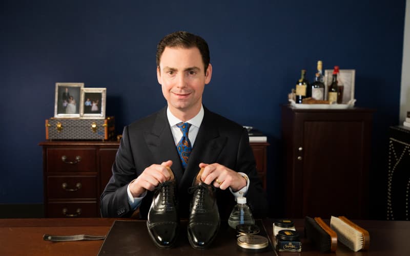 Kirby Allison smiling as he lifts a pair of polished shoes