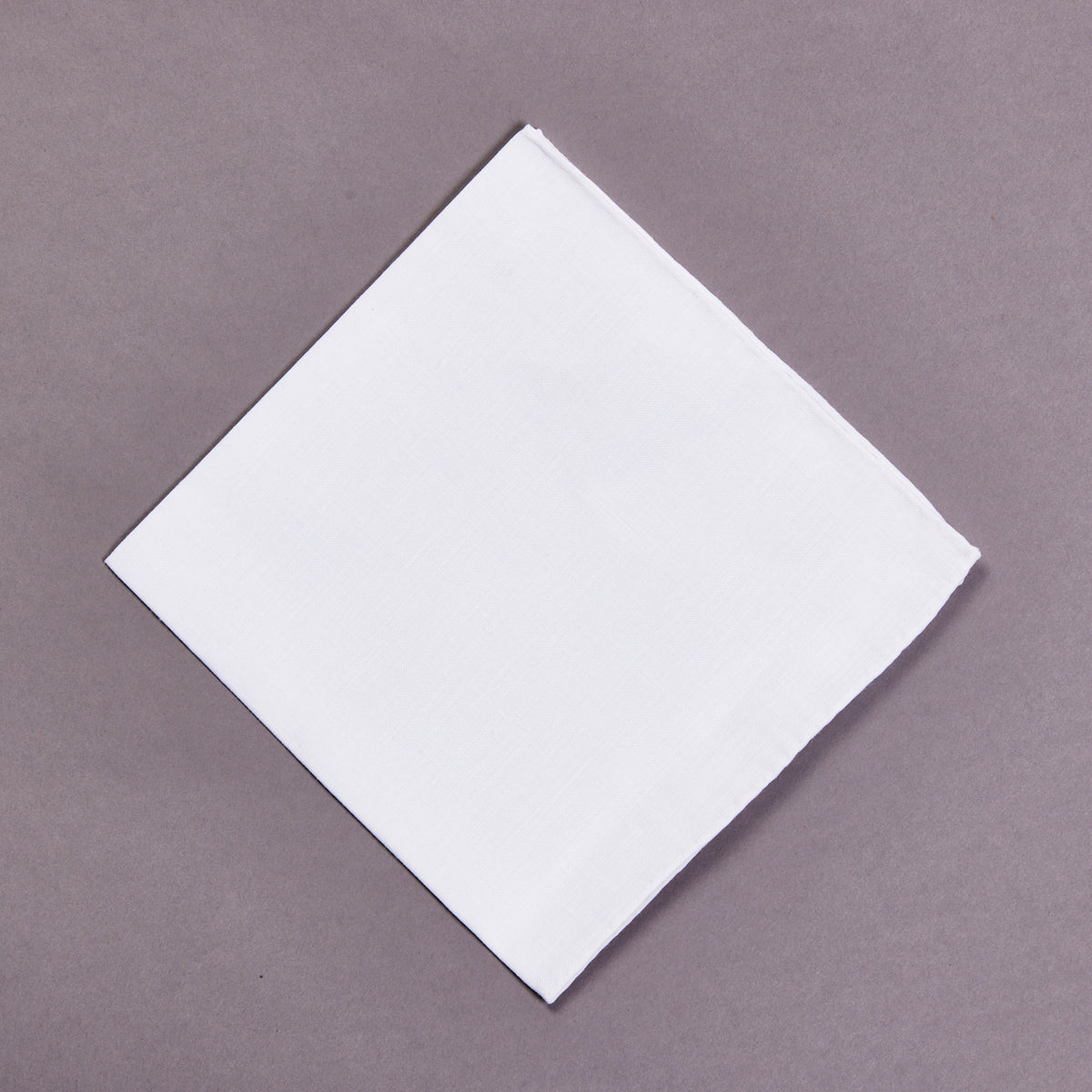 A Simonnot Godard 100% Linen Plain White Pocket Square on a gray surface.
