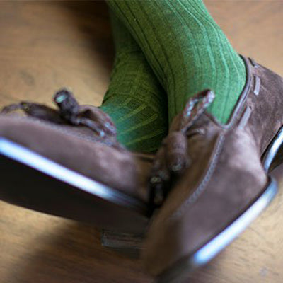 Close up image of a person's feet and ankles, wearing bright green dress socks and a pair of brown suede loafers. 