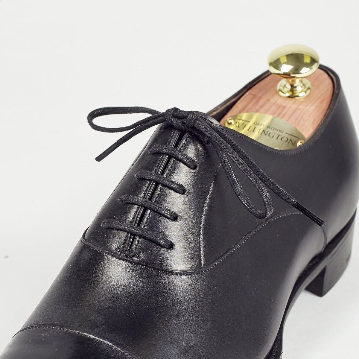 A black oxford shoe with Wellington Flat Waxed Dress Shoelaces from KirbyAllison.com on a white background.