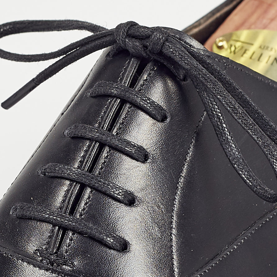 A close up of a black oxford dress shoe with KirbyAllison.com Wellington Flat Waxed Dress Shoelaces.