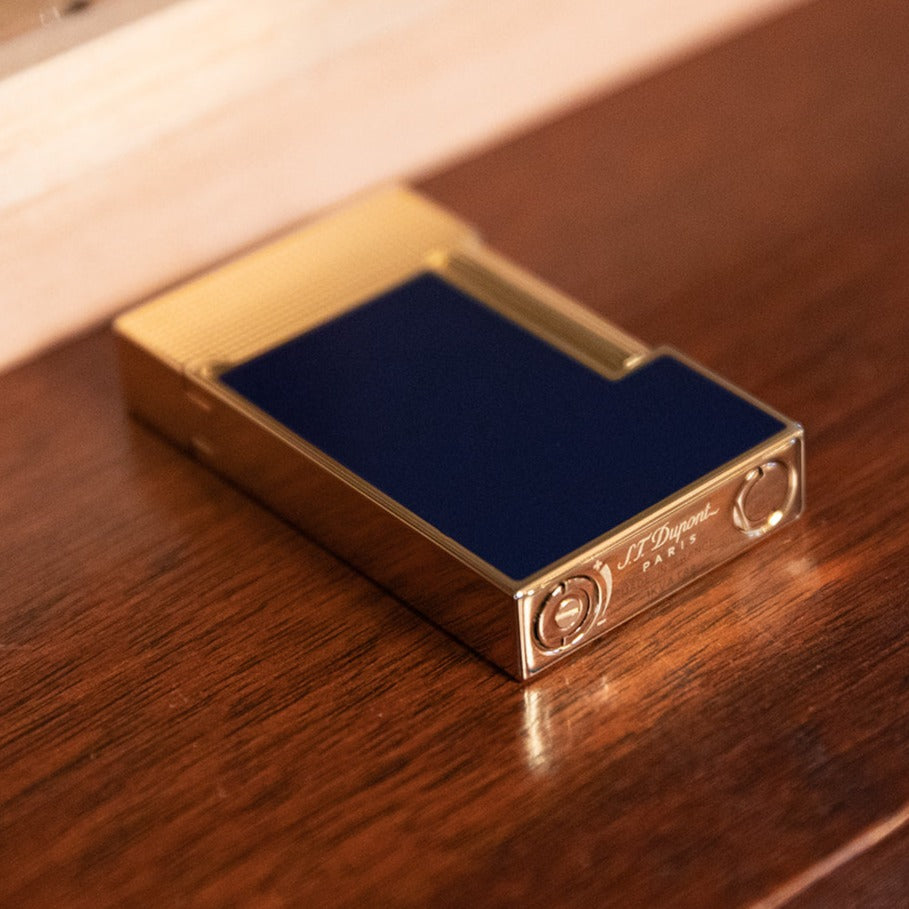 An S.T. Dupont Line 2 Gold Blue Lacquer Lighter with a blue lacquer finish sitting on top of a wooden table.