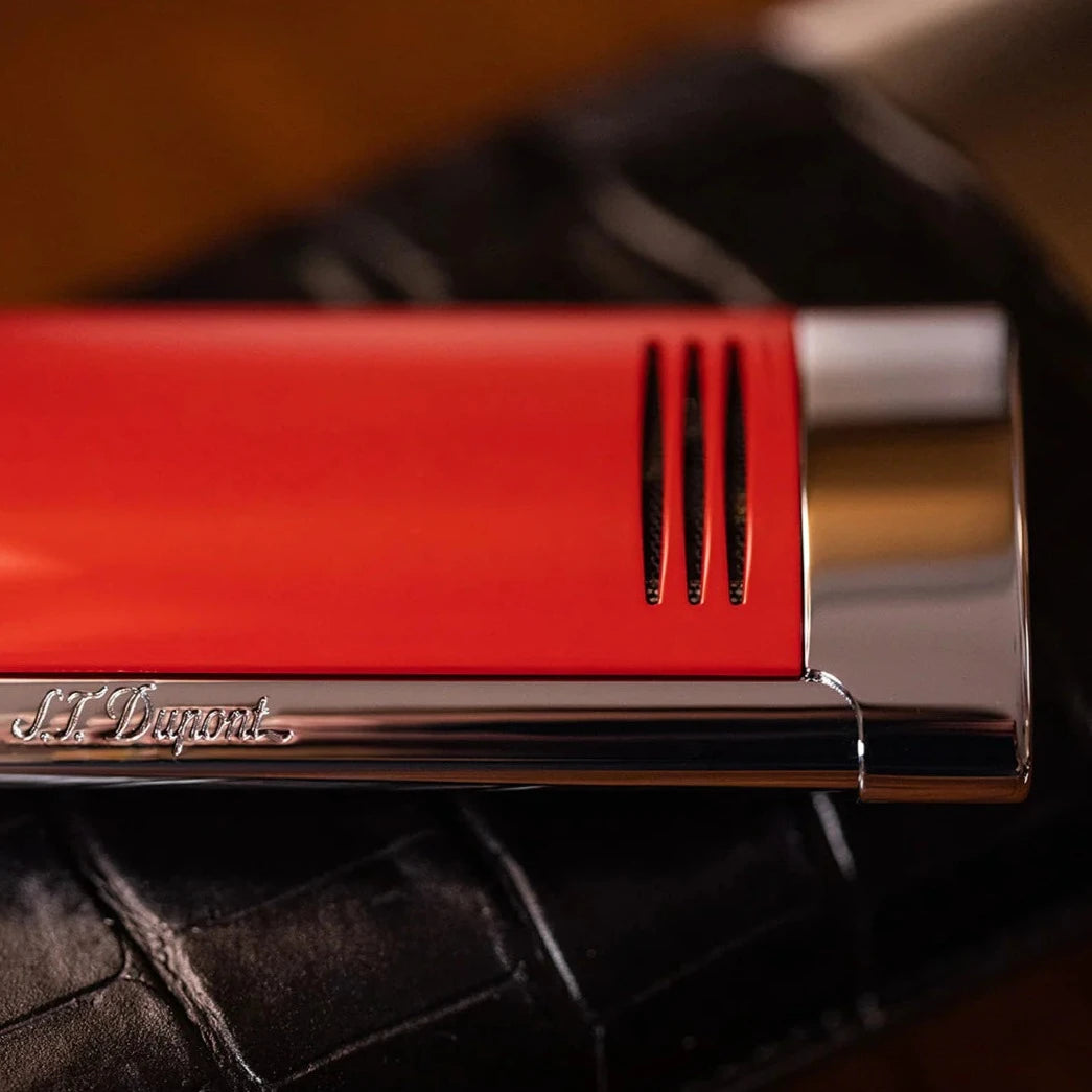 An S.T. Dupont Red and Chrome Megajet Lighter sits on top of a leather bag.