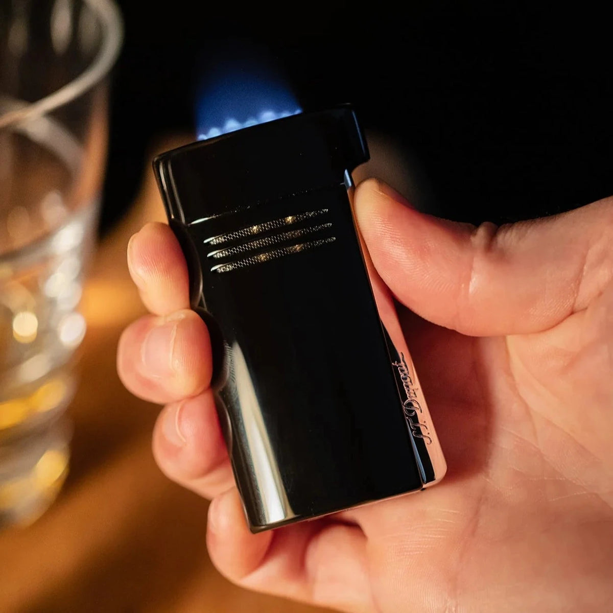 A person demonstrating S.T. Dupont Black Megajet Lighter performance by holding it next to a glass of wine.