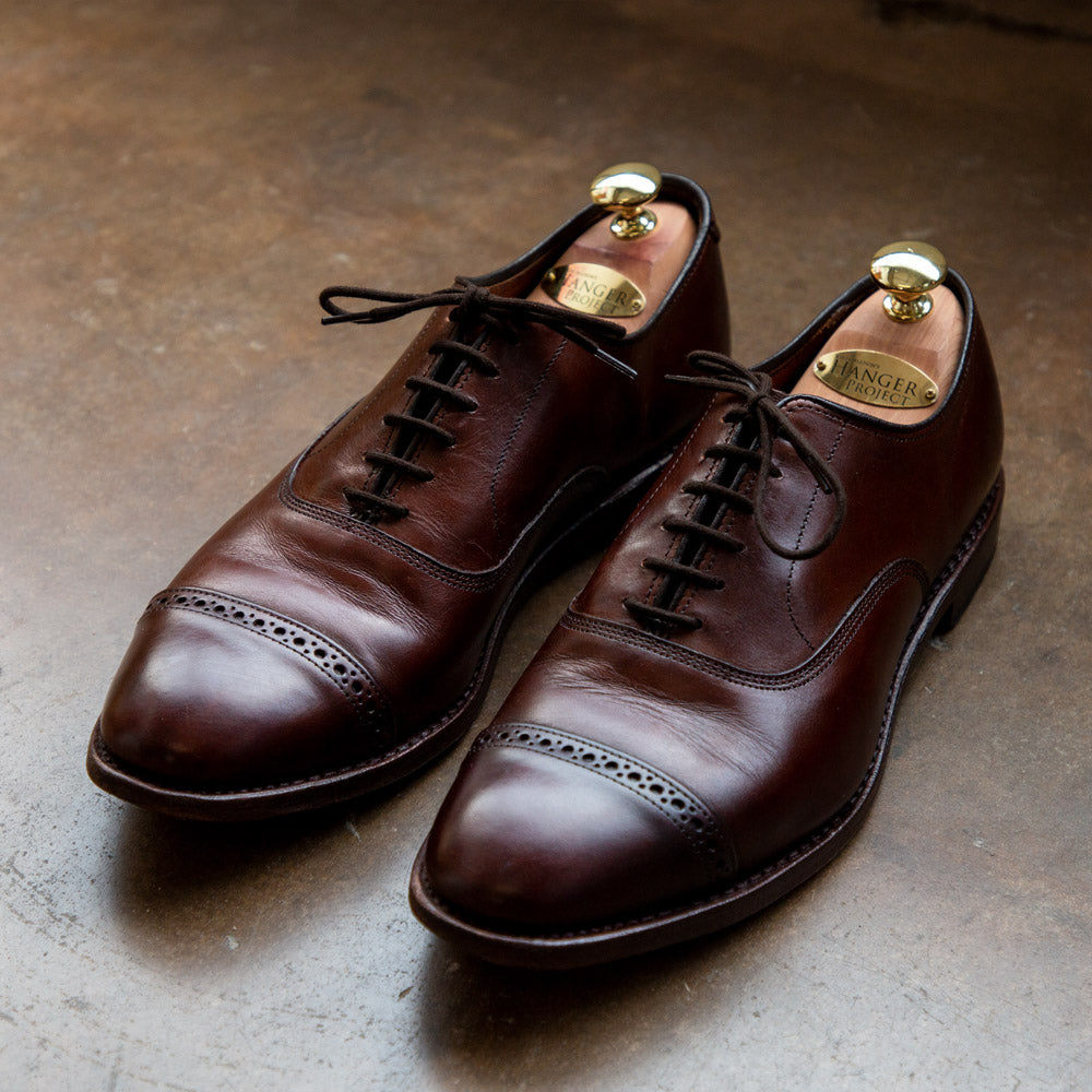 A pair of Kirby Allison Certified Restoration and Refurbishment brown oxford shoes on a concrete floor.