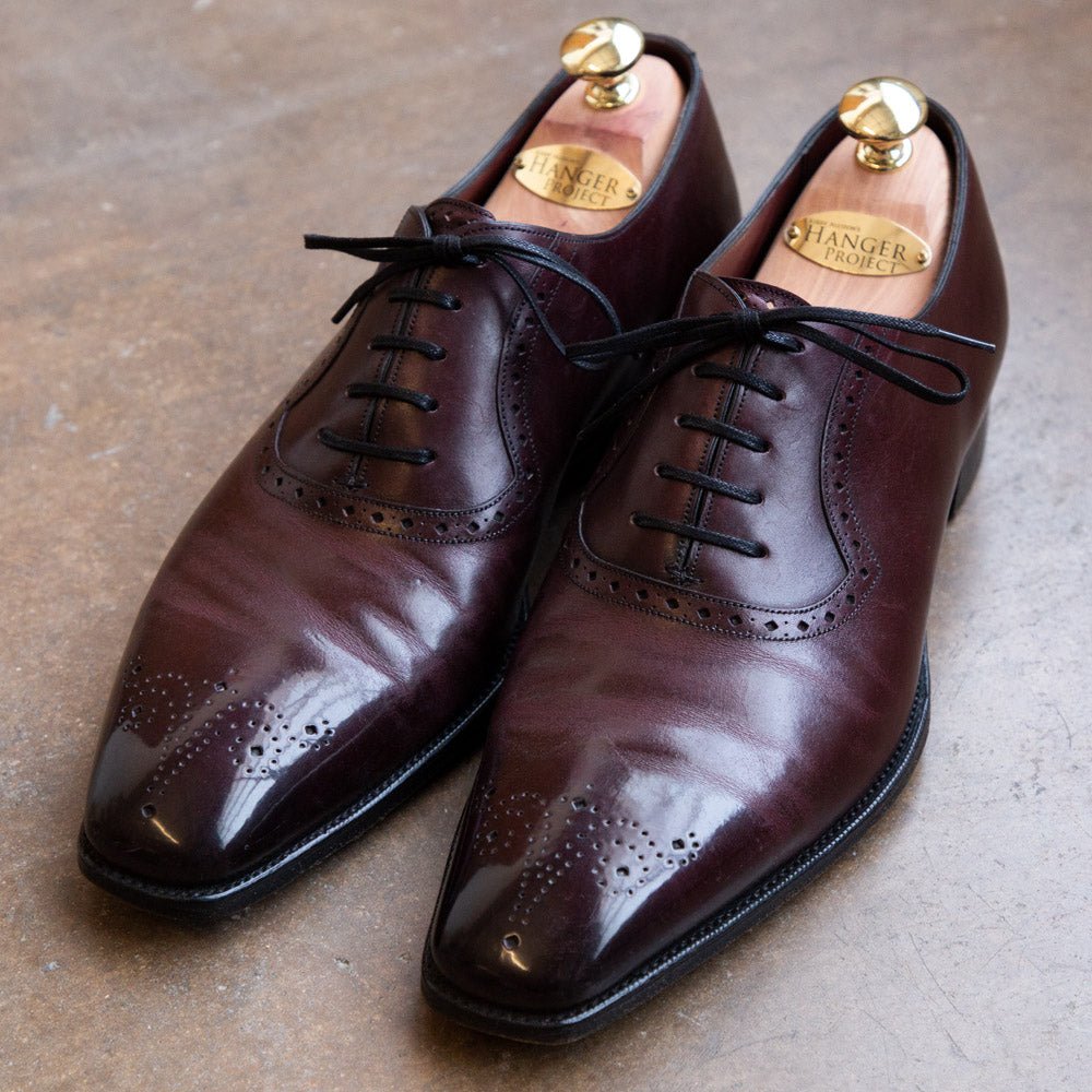 A pair of Kirby Allison Sovereign Grade Restoration and Refurbishment oxford shoes with JR Rendenbach oak-bark tanned outsoles lay on a concrete floor, showcasing the highest-quality workmanship.