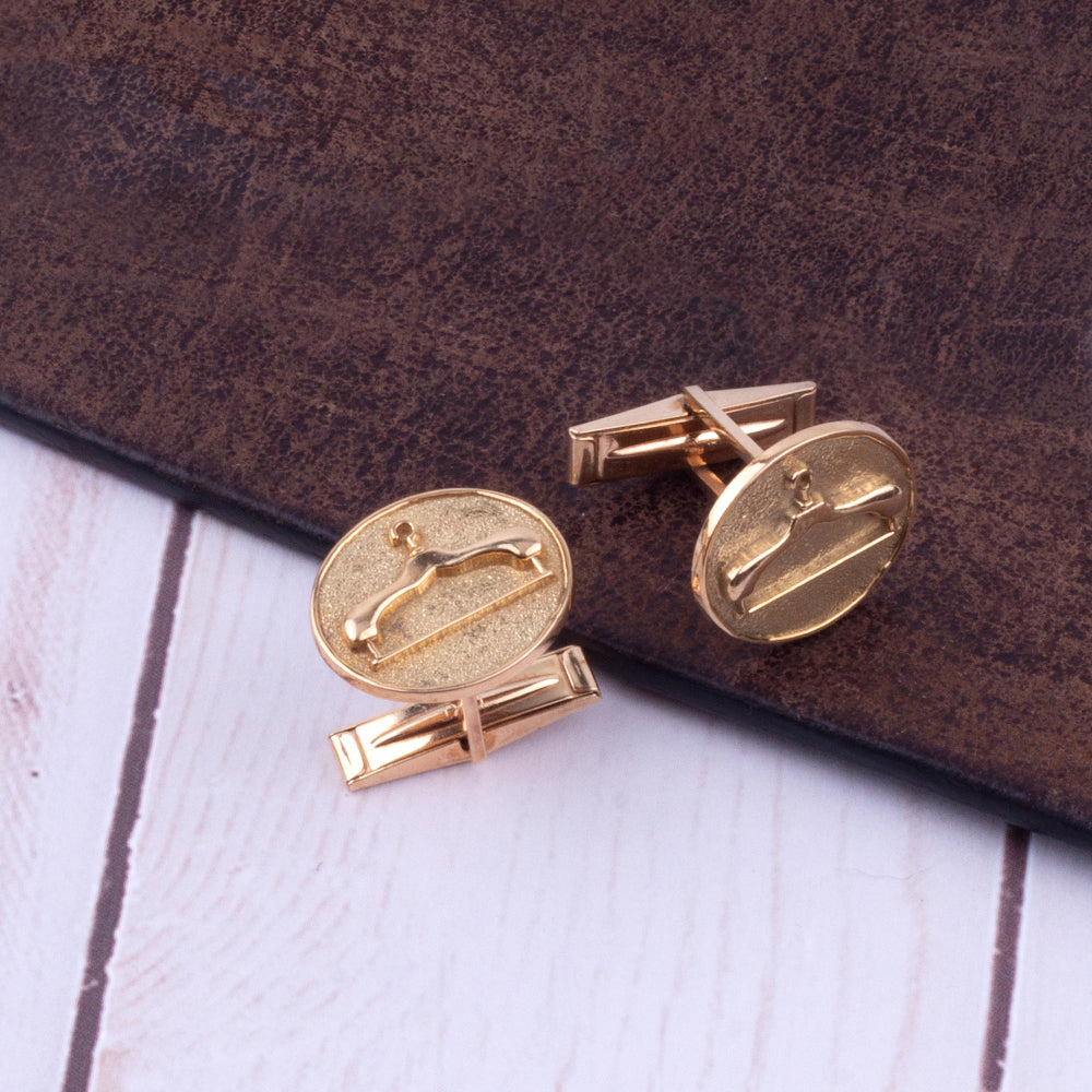 A pair of KirbyAllison.com Sovereign Grade Gold Hanger Cufflinks made of 14 kt gold on a wooden surface.