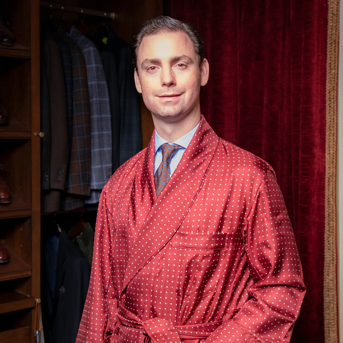 A man wearing a Sovereign Grade Burgundy London Dot Dressing Gown from KirbyAllison.com standing in a closet.