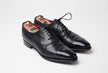 A pair of black oxford shoes on a white background showcasing the KirbyAllison.com Presidential Shoe Shine Service.